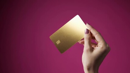 Female hand gently holding gleaming gold credit card against vibrant magenta backdrop, representing luxury, financial power, and sophisticated banking experience