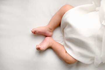 Top view of infant legs and feet wrapped in a white blanket on a clean bed. Minimal style with wide copy space—perfect for parenting ads, nursery brands, pediatric care, and baby products.