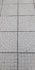 A top-down view of a city sidewalk with a geometric paving pattern of concentric circles. An abstract urban background for design, construction, and concepts of order.