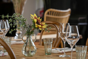 Elegant dinner table with sunflower (Helianthus annuus). Wooden served table ready for guests. Wooden decorated table with glasses, forks, napkin. 