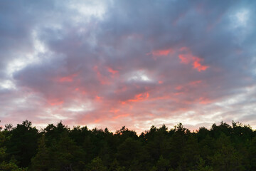 A fiery red sunset sky with dramatic storm clouds over a silhouetted northern forest skyline at dusk in twilight.