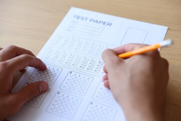 Student filling out multiple choice test at wooden table, closeup. Passing exam