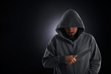 Criminal in hood with knife on dark background. Space for text