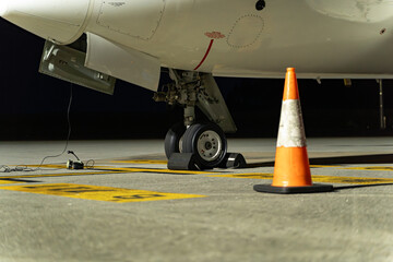 Airplane wheel on the runway waiting for takeoff, it is nighttime and the light is artificial. You can see some headsets on the ground that the coordinator uses to communicate with the pilot.