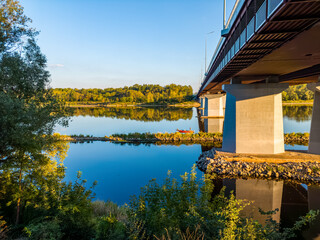 View from the Vistula riverbank under a large highway bridge, with people fishing from a red  boat.