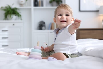 Fototapeta premium Cute little baby playing with toy pyramid on bed at home