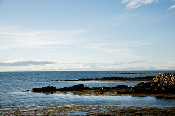 Serene coastal landscape with rocky shore and open sea under clear skies, Iceland