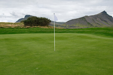 Scenic golf course with mountains, green field, and flag in Iceland countryside