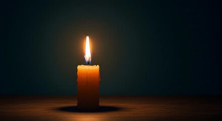 A lit candle on a wooden surface against a dark background.