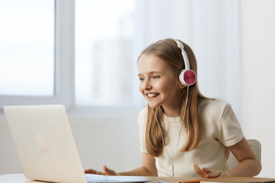 Young girl with headphones smiling at laptop, engaged in online learning or video call, bright and modern interior, seasonal vibes of productivity and happiness