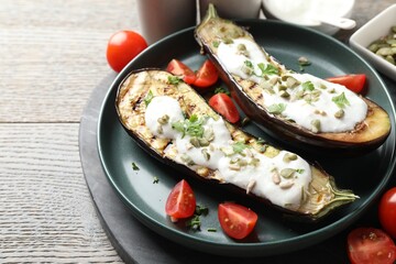 Slices of grilled eggplant with pumpkin seeds, tomatoes and yoghurt on wooden table, closeup