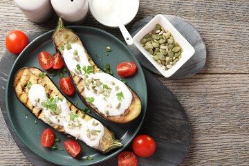 Slices of grilled eggplant with pumpkin seeds, tomatoes and yoghurt on wooden table, flat lay