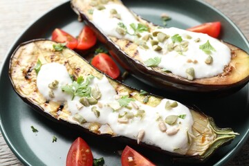 Slices of grilled eggplant with pumpkin seeds, tomatoes and yoghurt on wooden table, closeup
