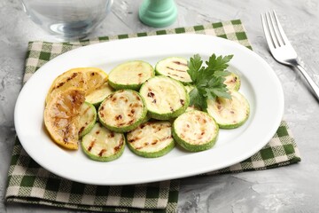 Delicious fried courgette slices with lemon and parsley served on grey table, closeup