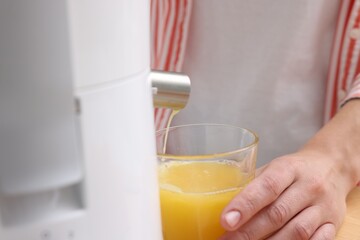 Woman making fresh orange juice with modern juicer indoors, closeup