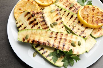 Delicious grilled courgette slices with pumpkin seeds, lemon and parsley on grey table, above view