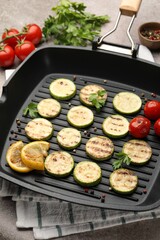Delicious grilled courgette slices with tomatoes, lemon and parsley in pan on grey textured table, closeup