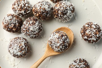 Tasty chocolate candies with nuts and coconut flakes on plate, top view