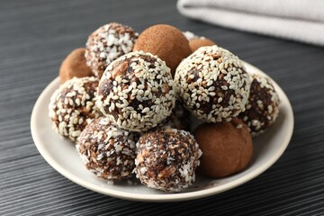 Tasty chocolate candies with cocoa powder, nuts and sesame seeds on black textured table, closeup