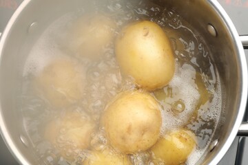 Young potatoes boiling in pot on stove, closeup