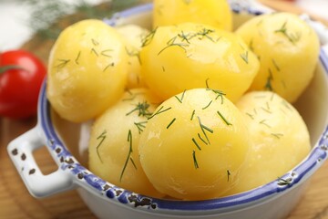 Tasty young boiled potatoes with dill and oil in bowl on wooden board, closeup