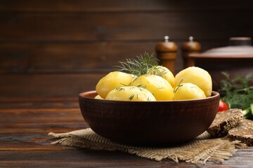 Tasty young boiled potatoes with dill and oil in bowl on wooden table, closeup. Space for text
