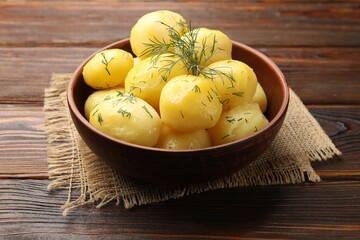 Tasty young boiled potatoes with dill and oil in bowl on wooden table, closeup