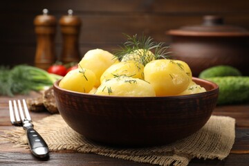 Tasty young boiled potatoes with dill and oil in bowl on wooden table, closeup