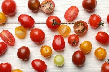 Different ripe tomatoes on white wooden table, flat lay