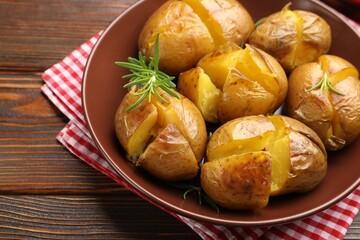 Tasty baked potatoes with rosemary served on wooden table, closeup