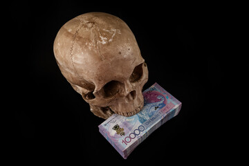 A stack of 10,000 Kazakhstani tenge bills in the teeth of a human skull on a black background