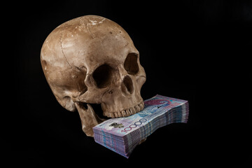 A stack of 10,000 Kazakhstani tenge bills in the teeth of a human skull on a black background