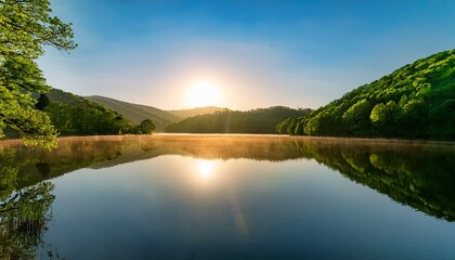 sunrise over a calm lake reflecting the lush green trees and hills