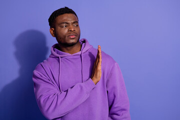 Confident young man gesturing stop in stylish purple hoodie on plain violet background demonstrating casual fashion trend