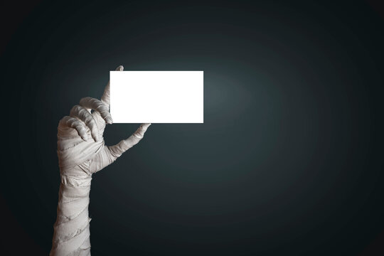 Mummy's hand wrapped in bandages holding blank sign template sheet of paper with empty copy space. Isolated background. Horrible risen dead mummy monster for a Halloween horror concept - Powered by Adobe