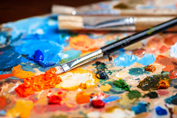 Obraz premium Old used brushes in an artist's studio, palette with multi-colored spots of oil or acrylic paint