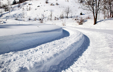 Obraz premium vehicle trace in fresh snow on a rural turned road crossing snowy mountain in the French Alps