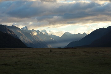 Dramatic light pierces through clouds, illuminating snow-capped mountains above golden plains near Mount Sunday, Canterbury Plains, New Zealand, on May 18, 2025. A majestic Lord of the Rings landscape