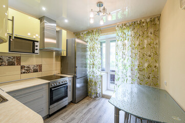 brightly lit kitchen features yellow cabinets, stainless steel appliances, floral curtains, and a glass-top table