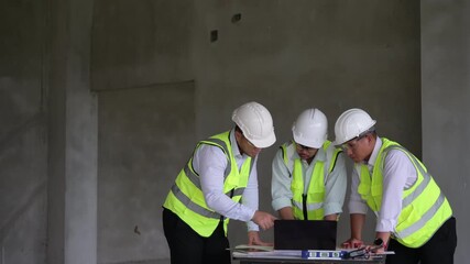 Three construction engineers collaborating on-site using a laptop and tablet while discussing project plans in an unfinished building. Ideal for smart construction and teamwork concepts.
