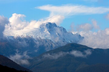Mount Tasman rises above forested hills and clouds in South Island, New Zealand. Captured during road trip on May 16, 2025. Serene and dramatic alpine landscape.