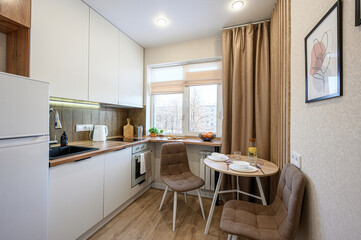 cozy kitchen with white cabinets, wooden accents, a dining table set for two, and natural light