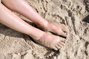 Sand-covered feet sink into sunlit beach, capturing relaxed moment. Soft texture of sand contrasts with smooth skin. Warm lighting evokes sense of tranquility