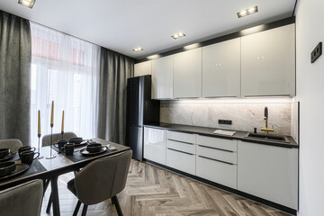 Modern kitchen with sleek white cabinets, black accents, and a dining area set for a meal. Natural light floods the space through sheer curtains