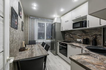 modern kitchen features a wooden table with black chairs, a stainless steel refrigerator, white cabinets, and a countertop with a marbled pattern. Recessed lighting brightens the room