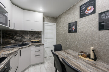 Modern kitchen featuring white cabinets, dark countertop, wooden table with black chairs, and coffee-themed wall art