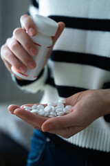Female pouring pills from white plastic bottle into hand, symbolizing healthcare and supplements. 