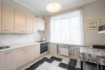 cozy kitchen features light wood cabinets, a black and white tiled floor, and a bright window with sheer curtains. A table sits near the window