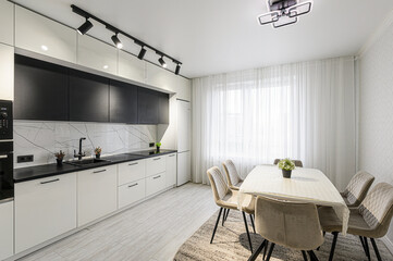 bright kitchen features a modern design with black and white cabinetry, marble backsplash, a dining table with chairs, and ample natural light from a large window