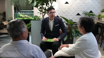 Professional financial advisor explaining retirement plan to happy senior Asian couple using digital tablet. Insurance agent consulting elderly clients about investment in modern office. - Powered by Adobe